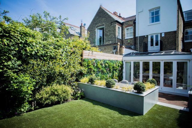 A family garden with terrace constructed with Design Clad from London Stone and VistaGreen artificial green wall panels to enhance a small well-loved garden.