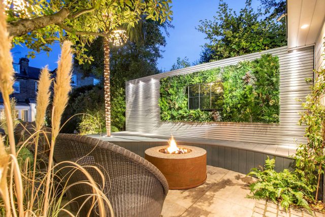 A family garden with terrace constructed with Design Clad from London Stone and VistaGreen artificial green wall panels to enhance a small well-loved garden.