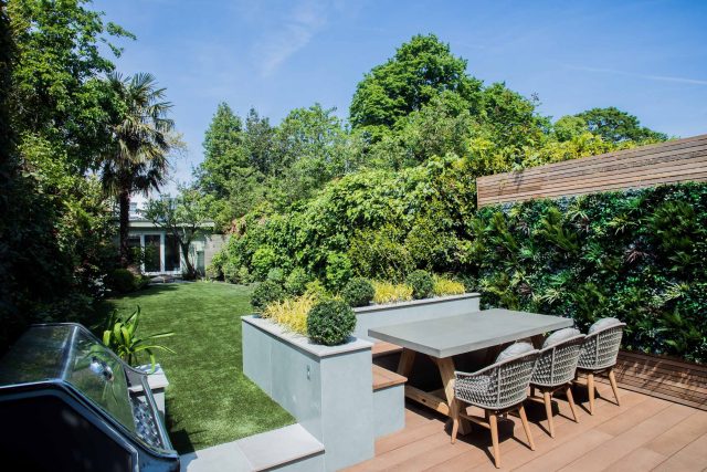 A family garden with terrace constructed with Design Clad from London Stone and VistaGreen artificial green wall panels to enhance a small well-loved garden.