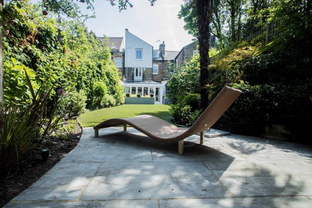 A family garden with terrace constructed with Design Clad from London Stone and VistaGreen artificial green wall panels to enhance a small well-loved garden.