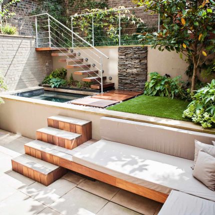 City design jacuzzi garden low maintenance with artificial lawn, stacked stone water wall BBQ Fire place feature, Hampstead Village, natural stone led lighting.