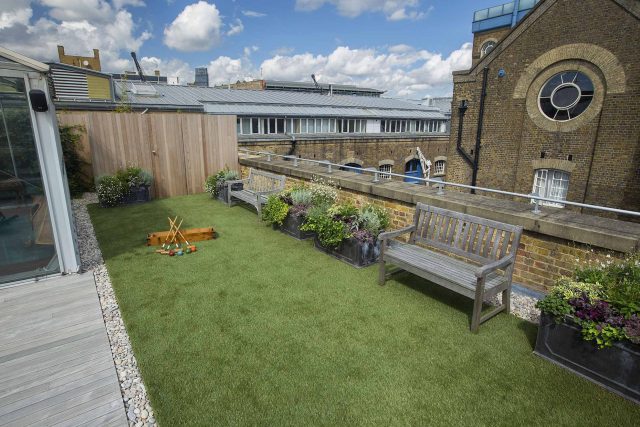 Roof terrace with decking, artificial level lawn and LED lighting design at New Concordia Wharf, highlight surfaces and architectural elements in the evenings.