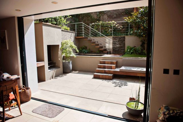 City design jacuzzi garden low maintenance with artificial lawn, stacked stone water wall BBQ Fire place feature, Hampstead Village, natural stone led lighting.