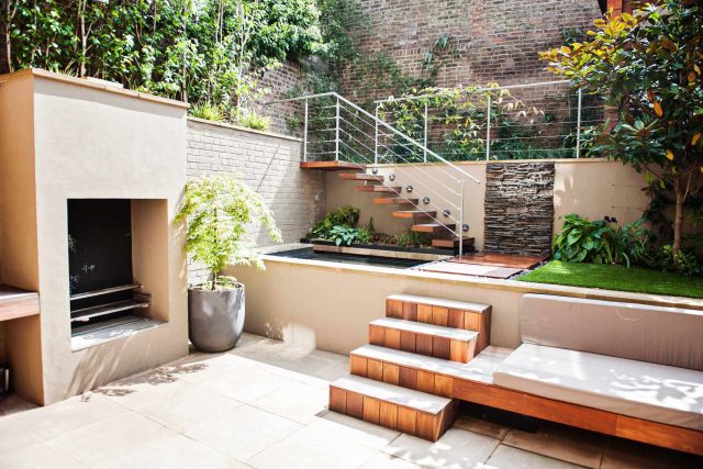 City design jacuzzi garden low maintenance with artificial lawn, stacked stone water wall BBQ Fire place feature, Hampstead Village, natural stone led lighting.