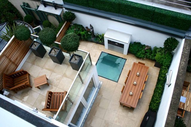 Small city garden design Knightsbridge with bespoke flambeaux fire burner and neat clipped planting, teak furniture parasol, clipped plants Hunza light fittings.