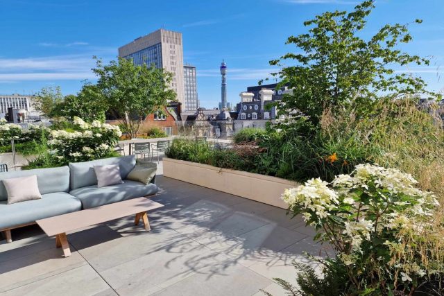 A grey sectional sofa is positioned next to a stone planter with hydrangeas in modern London.