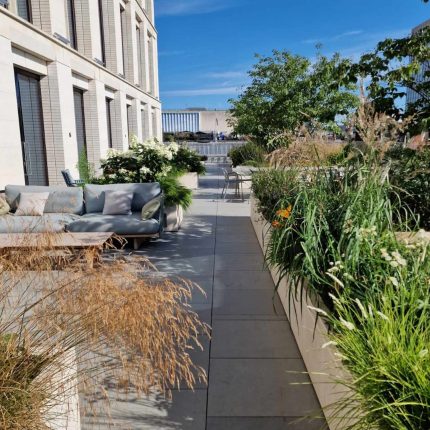 A luxury modern rooftop terrace featuring a stone pathway, a sofa, and planters.