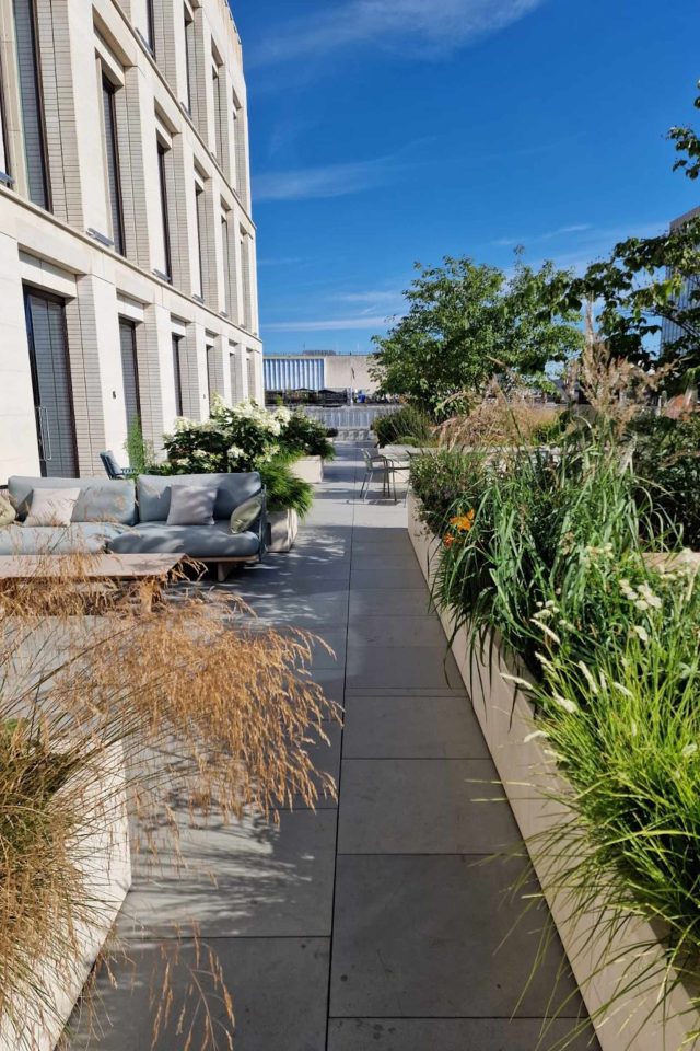 A luxury modern rooftop terrace featuring a stone pathway, a sofa, and planters.