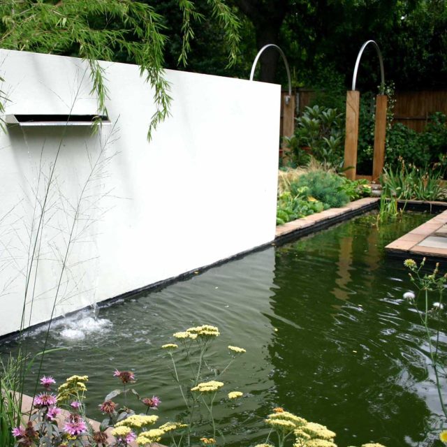 A minimalist pond with a water spout, ceramic urn, and grasses in a contemporary design.