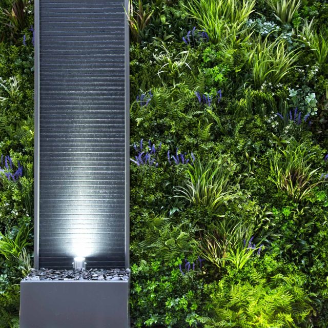 Small courtyard garden transformed with artificial green wall panels and a focal ribbed slate stone water feature, planting, natural light, small garden space.