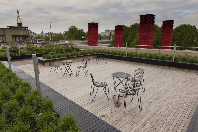 A modern London rooftop terrace with a wooden deck and wire furniture.