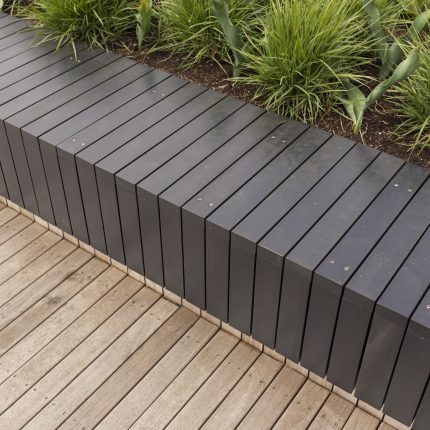 A slat bench, retaining wall, and wooden decking with ornamental grass.