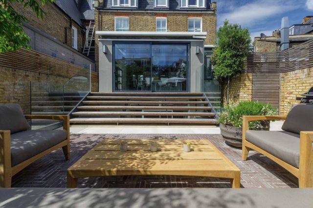 Courtyard Garden Design with an elegant walled space with Yorkstone work Fulham by The Garden Builders, canopy shade for a central lounge planted seating area.