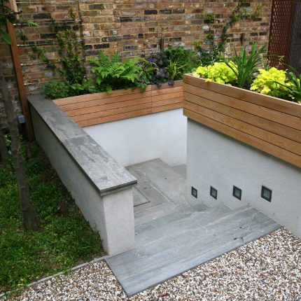Gravel small town garden Chelsea with a beautiful water feature, acer planters landscaper designers with horizontal timber cladding by Edlis Design Associates.