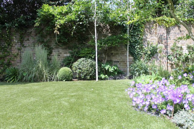 An artificial lawn features a boxwood topiary and a brick wall in luxury Wimbledon.