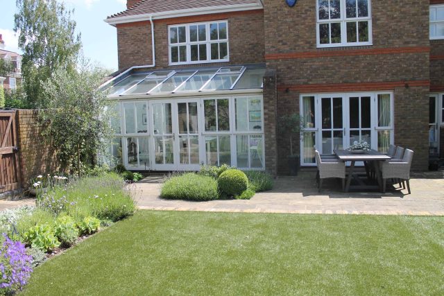 An artificial lawn stretches from a conservatory to a York stone patio in luxury Wimbledon.