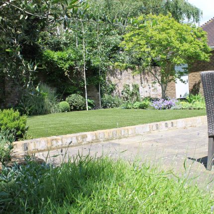 An artificial lawn and York stone paving are framed by a brick wall in luxury Wimbledon.