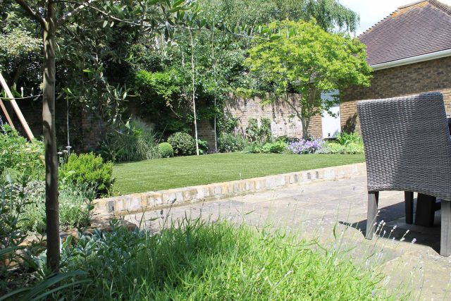 An artificial lawn and York stone paving are framed by a brick wall in luxury Wimbledon.