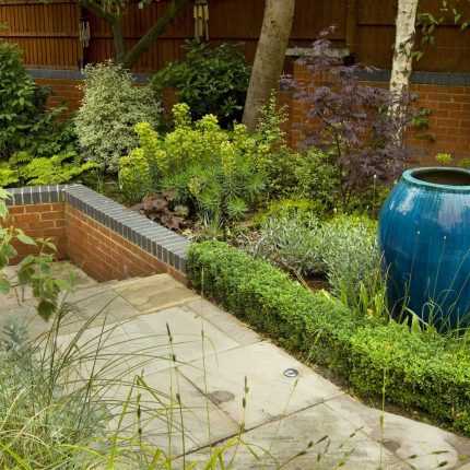 Large paved garden terrace with sunken sandstone paved area, comfortable outdoor sofa by landscaping design company, raised timber decking, Garden Builders.
