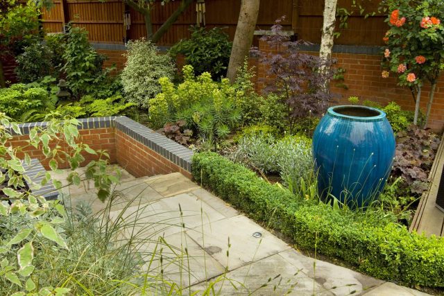 Large paved garden terrace with sunken sandstone paved area, comfortable outdoor sofa by landscaping design company, raised timber decking, Garden Builders.