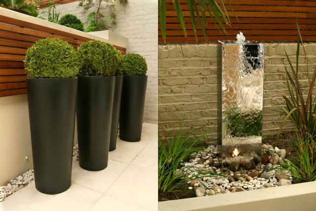 A boxwood topiary in a black planter next to a stainless steel fountain.