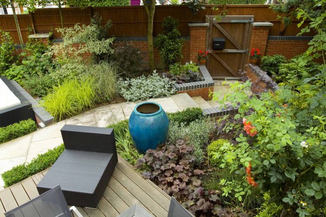 Large paved garden terrace with sunken sandstone paved area, comfortable outdoor sofa by landscaping design company, raised timber decking, Garden Builders.