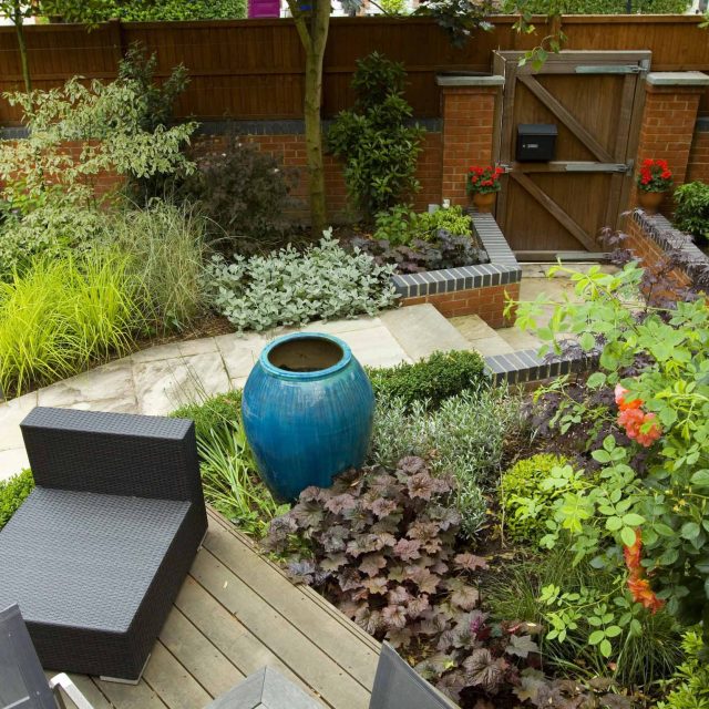 Large paved garden terrace with sunken sandstone paved area, comfortable outdoor sofa by landscaping design company, raised timber decking, Garden Builders.