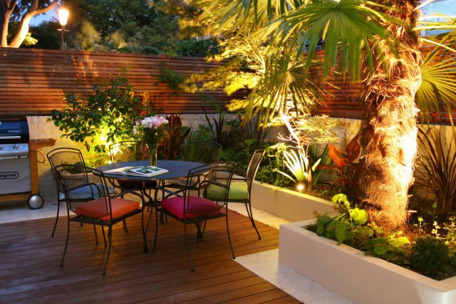 A hardwood deck and patio area featuring a dining set, palm tree, and slatted fence.