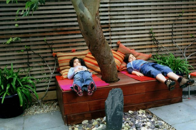 Child friendly synthetic lawn designed as a low-maintenance, contemporary and colourful space, planted raised beds slate terrace hardwood tree seat specialists.