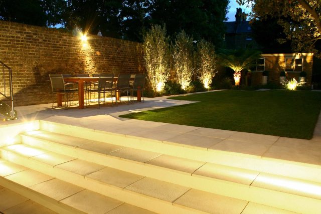 Modern Family Garden in Battersea with patio lighting planting and machined sandstone pathway specialist company stone work, planting herbaceous perennials.