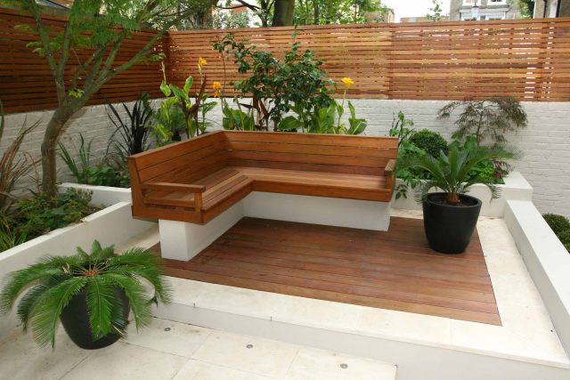 An L-shaped wood bench and slatted fence on a modern patio deck.