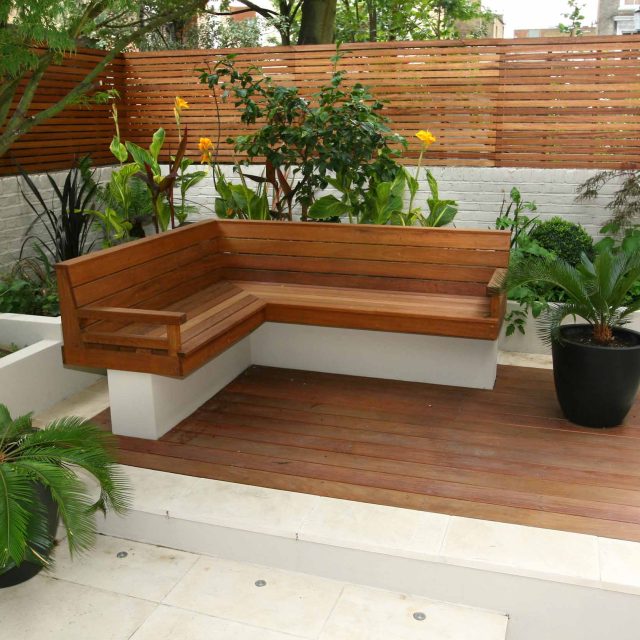 An L-shaped wood bench and slatted fence on a modern patio deck.