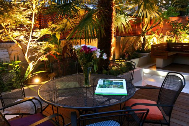 A patio deck with a dining set and an illuminated hardwood slat fence.