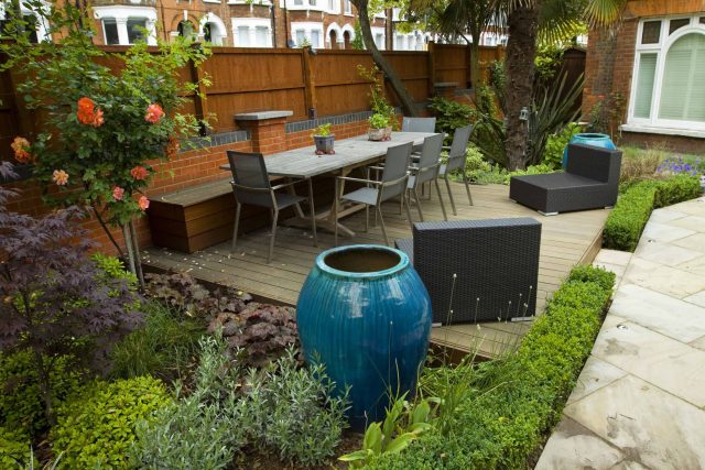 Large paved garden terrace with sunken sandstone paved area, comfortable outdoor sofa by landscaping design company, raised timber decking, Garden Builders.