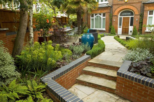 Large paved garden terrace with sunken sandstone paved area, comfortable outdoor sofa by landscaping design company, raised timber decking, Garden Builders.