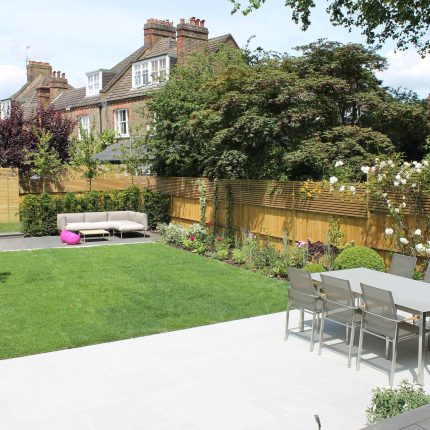 A modern sandstone patio features a lawn, a slatted timber fence, and a dining set.