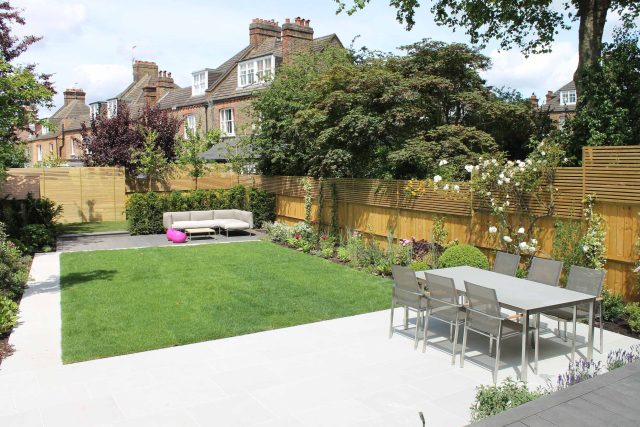 A modern sandstone patio features a lawn, a slatted timber fence, and a dining set.