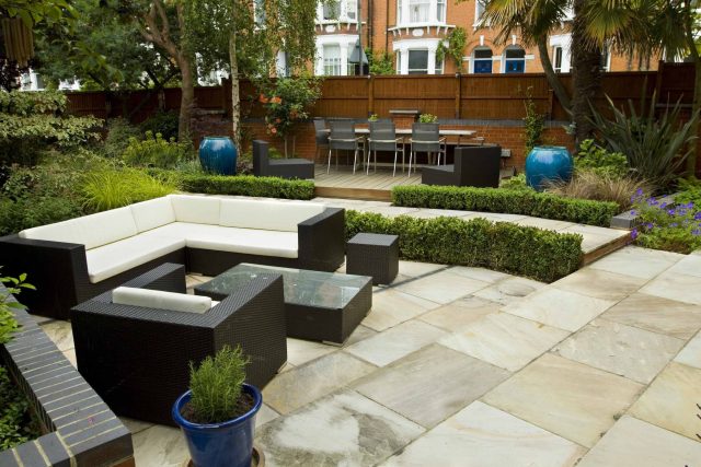 Large paved garden terrace with sunken sandstone paved area, comfortable outdoor sofa by landscaping design company, raised timber decking, Garden Builders.