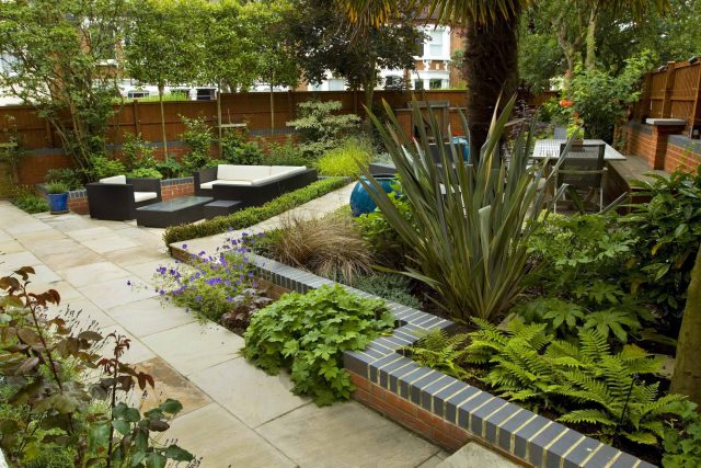 Large paved garden terrace with sunken sandstone paved area, comfortable outdoor sofa by landscaping design company, raised timber decking, Garden Builders.
