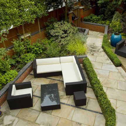 Large paved garden terrace with sunken sandstone paved area, comfortable outdoor sofa by landscaping design company, raised timber decking, Garden Builders.