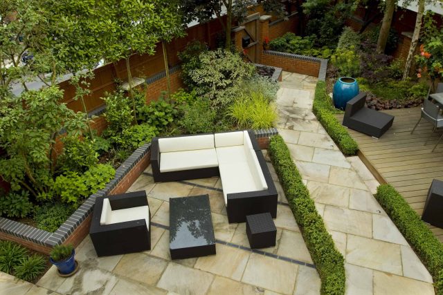 Large paved garden terrace with sunken sandstone paved area, comfortable outdoor sofa by landscaping design company, raised timber decking, Garden Builders.