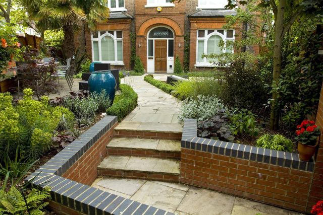 Large paved garden terrace with sunken sandstone paved area, comfortable outdoor sofa by landscaping design company, raised timber decking, Garden Builders.