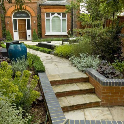 Large paved garden terrace with sunken sandstone paved area, comfortable outdoor sofa by landscaping design company, raised timber decking, Garden Builders.