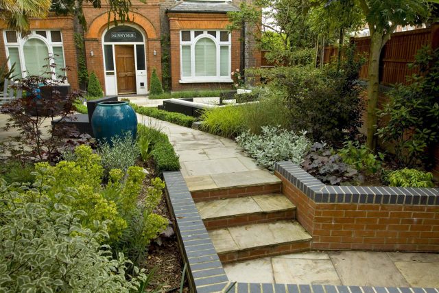Large paved garden terrace with sunken sandstone paved area, comfortable outdoor sofa by landscaping design company, raised timber decking, Garden Builders.