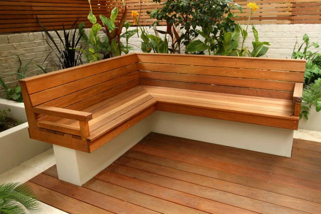 A slatted hardwood bench and concrete planter on a deck with canna lilies.
