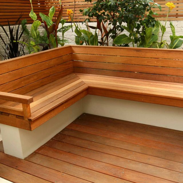 A slatted hardwood bench and concrete planter on a deck with canna lilies.