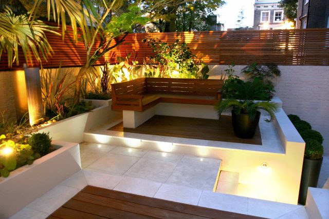 A slatted hardwood bench on limestone paving surrounded by a cycad and LED lighting.