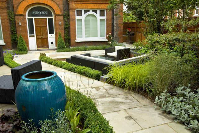 Large paved garden terrace with sunken sandstone paved area, comfortable outdoor sofa by landscaping design company, raised timber decking, Garden Builders.