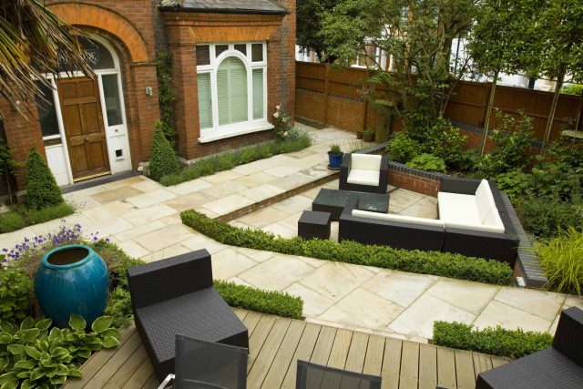 Large paved garden terrace with sunken sandstone paved area, comfortable outdoor sofa by landscaping design company, raised timber decking, Garden Builders.