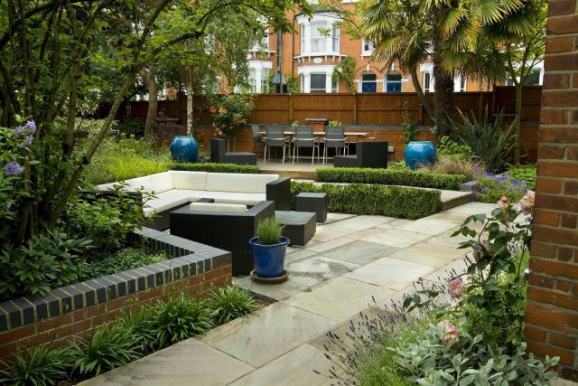 Large paved garden terrace with sunken sandstone paved area, comfortable outdoor sofa by landscaping design company, raised timber decking, Garden Builders.